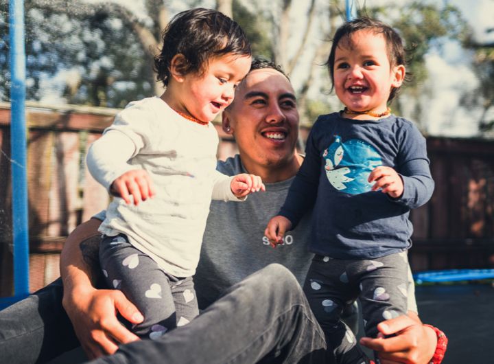 Family of Maori, Pacific Islander appearance, dad with two small children, smiling, outdoors